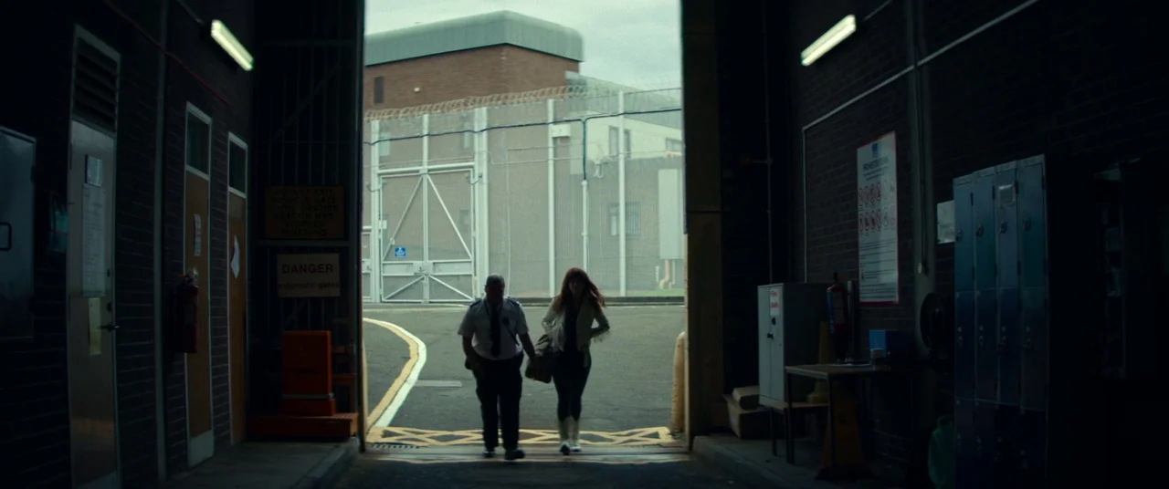 Wild Rose (2018) movie still: wide — A high-security facility entrance features a large vehicle gate and surrounding razor wire fencing. A security…
