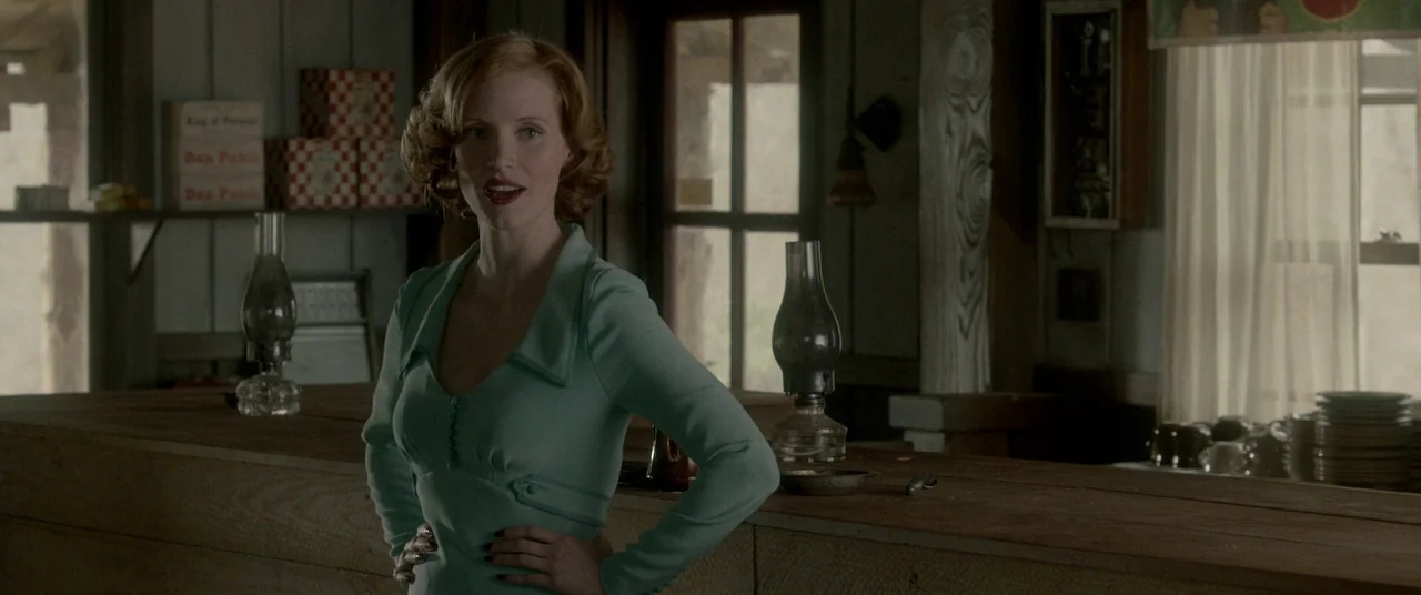 Lawless (2012) movie still: medium — A rustic general store interior features wooden counters and shelves filled with vintage products. A woman in a…