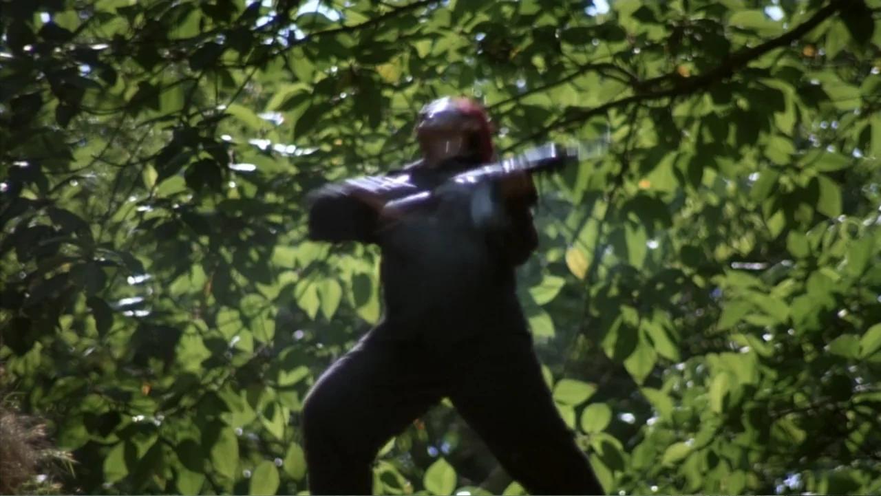 Behind Enemy Lines (2001) movie still: fullbody — A dense patch of woodland with sunlight filtering through a thick green canopy. A man stands in…