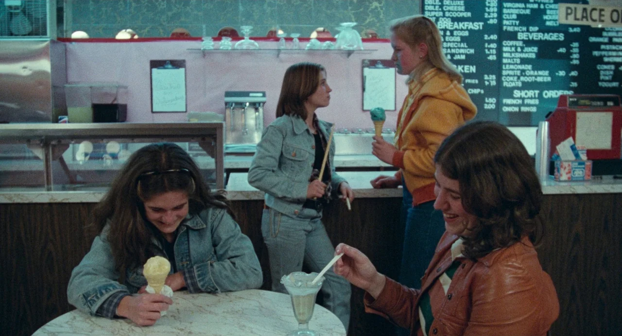 Out of the Blue (1980) movie still: medium — An ice cream parlor features a menu board on the wall and circular tables. Four teenage girls eat…