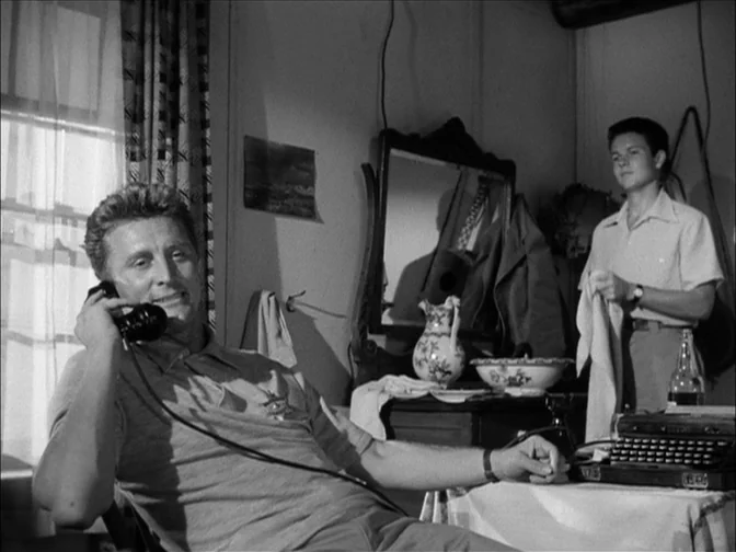 Ace In The Hole (1951) movie still: medium — A 1950s room features a desk with a vintage typewriter and a dressing table. One man sits using a…