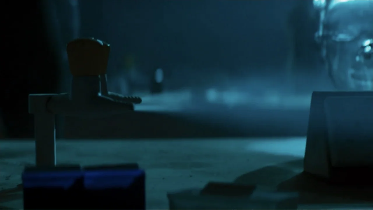 Robot Overlords (2015) movie still: medium — A dimly lit desk workspace features a mechanical desk object and a blurry background. Objects rest on a…
