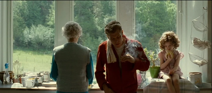 Mister Lonely (2007) movie still: medium — An interior space features a large window overlooking a verdant, sunlit outdoor area. An older woman, a…