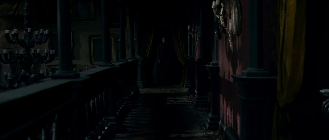 The Woman in Black (2012) movie still: wide — A dark, wood-paneled mansion corridor features ornate columns and walls lined with framed paintings. A…