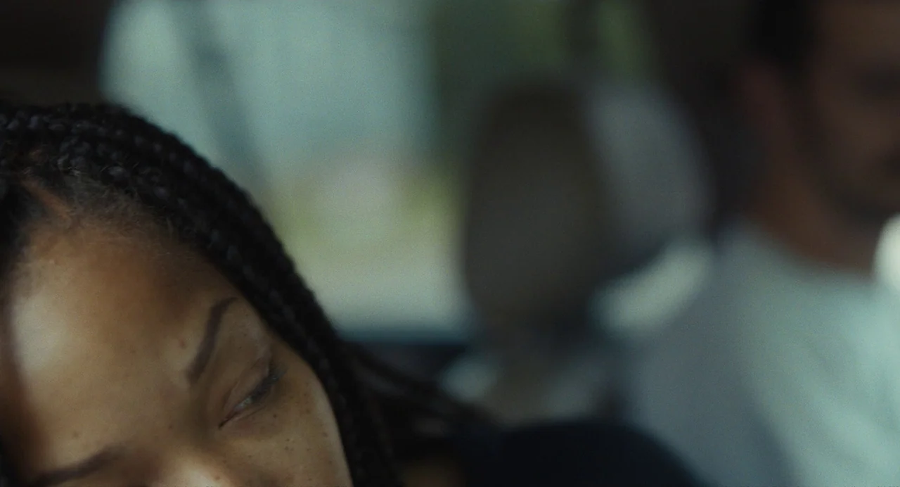 Test Pattern (2019) movie still: closeup — A close-up view inside a car shows a person with braided hair resting. The background is heavily out of…
