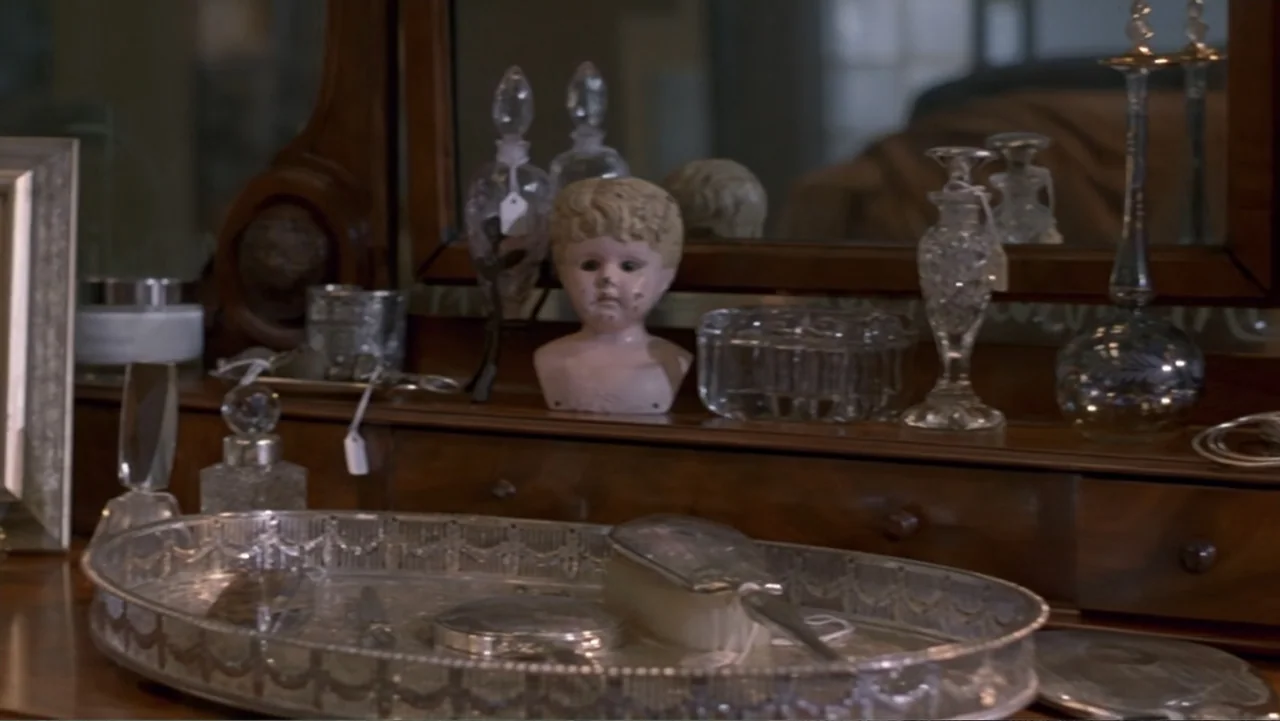 13 Ghosts (1960) movie still: medium — A dark wooden antique vanity table displays various vintage glass perfume bottles and tools. A pale doll head…