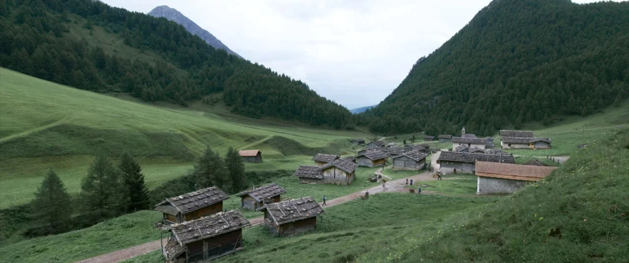A Hidden Life (2019) movie still: establishing — A rural alpine village of small wooden huts sits in a lush green valley. Surrounded by steep…
