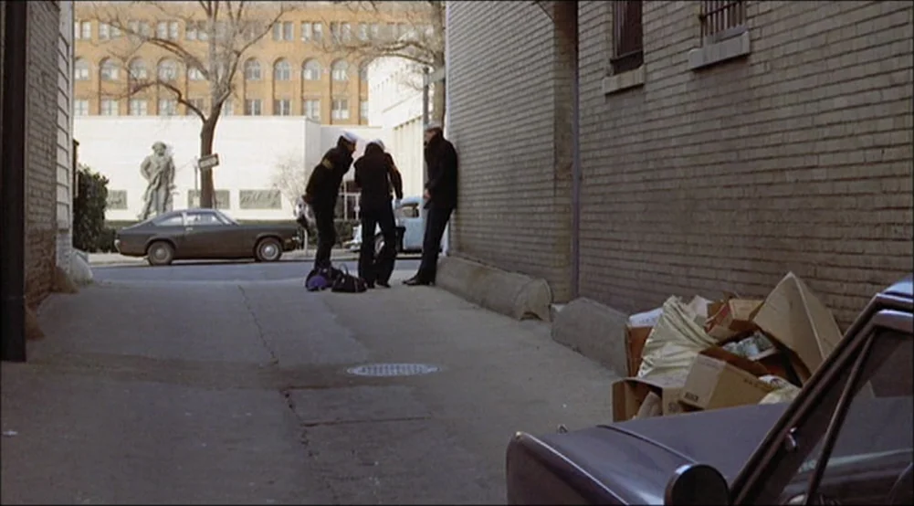 The Last Detail (1973) movie still: wide — A narrow brick alleyway contains a pile of cardboard boxes on the right side. Three individuals dressed…