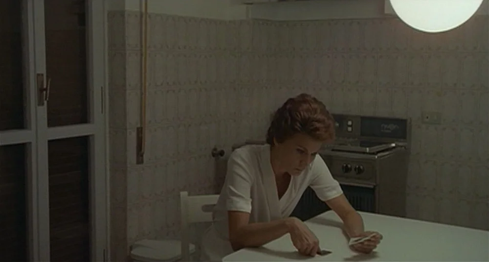 Footprints (Le Orme) (1975) movie still: medium — A quiet kitchen features light-colored grid-patterned wall tiles and a simple white table. A…