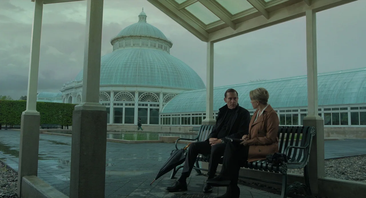 Gemini Man (2019) movie still: wide — A glass conservatory with a large central dome sits across a paved plaza. A man and a woman sit together on a…