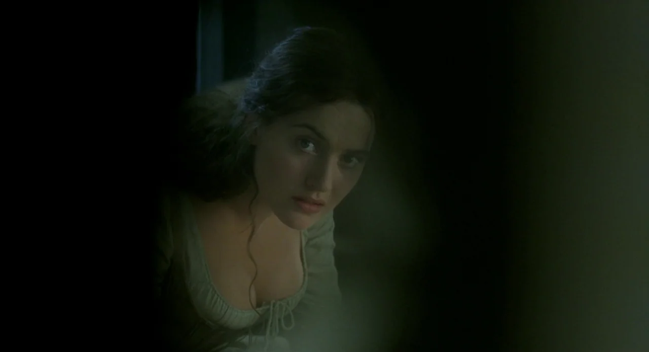 Quills (2000) movie still: closeup — A dark, dimly lit room with heavy shadows obscuring the background. A young woman in a period-style dress…