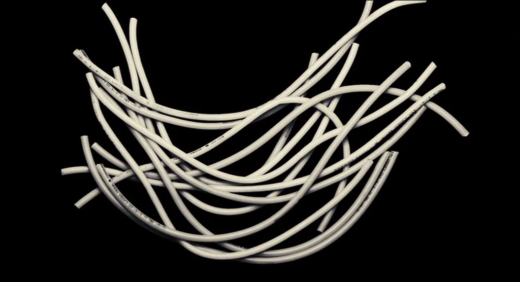 Sin City (2005) movie still: closeup — A cluster of curved, smooth white plastic tubes lies in a tangled heap. The objects are isolated against a…