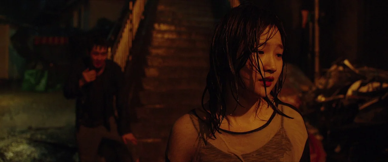 Parasite (2019) movie still: medium — A dark outdoor staircase at night is lit by ambient artificial yellow street lighting. A woman with wet hair…