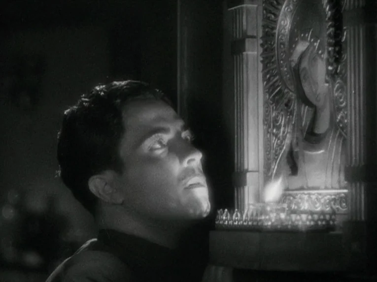 Mata Hari (1931) movie still: medium — A dark, quiet space featuring an Orthodox-style metallic icon mounted on a wall. A man gazes intently at the…