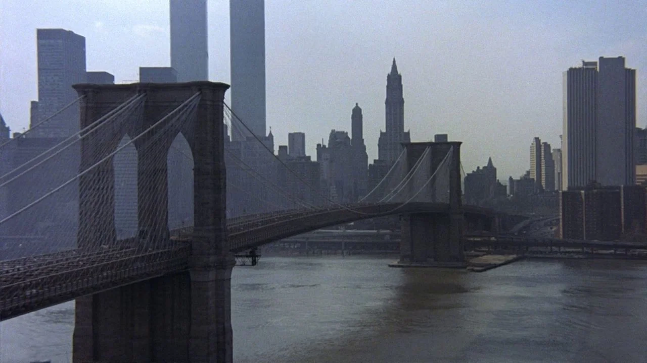 Saturday Night Fever (1977) movie still: establishing — The Brooklyn Bridge spans across the river with the Manhattan skyline visible behind it. The…