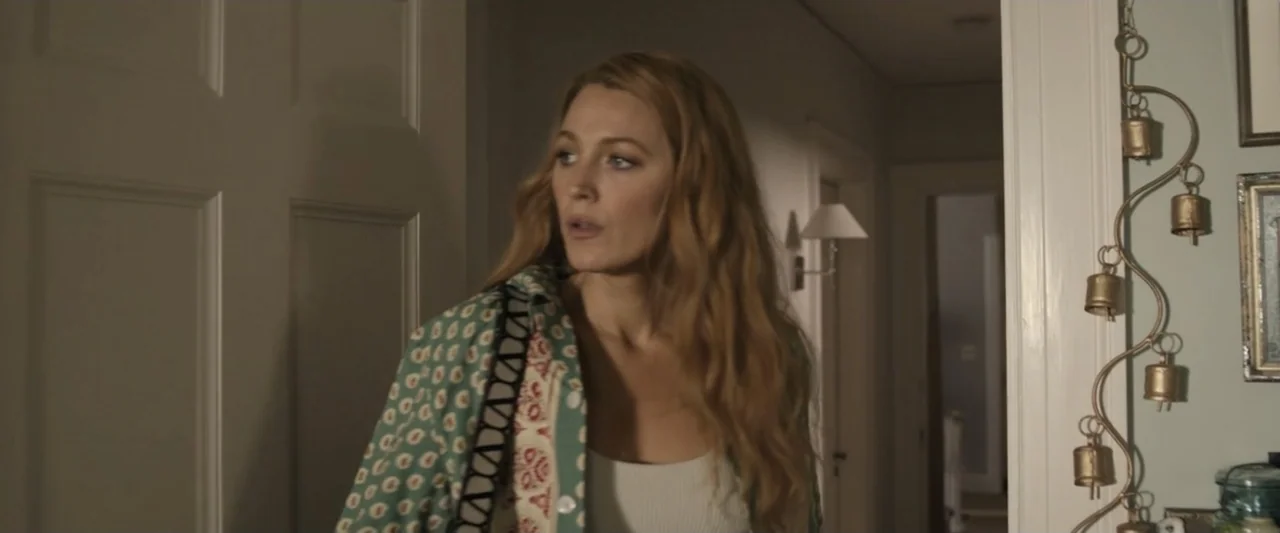 It Ends with Us (2024) movie still: medium — A residential hallway features white door frames and hanging brass bells on the wall. A woman with long…