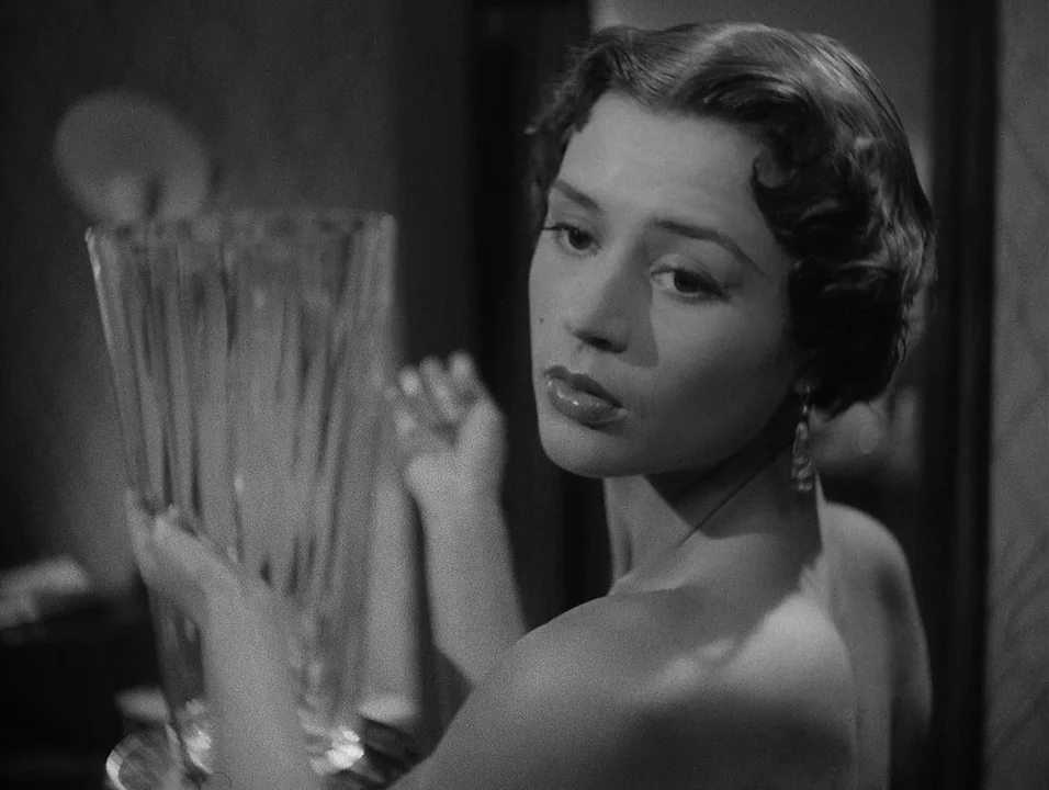 Dreams (1955) movie still: closeup — A dark indoor space featuring a reflective glass vase held by a young woman. The woman turns her head toward…