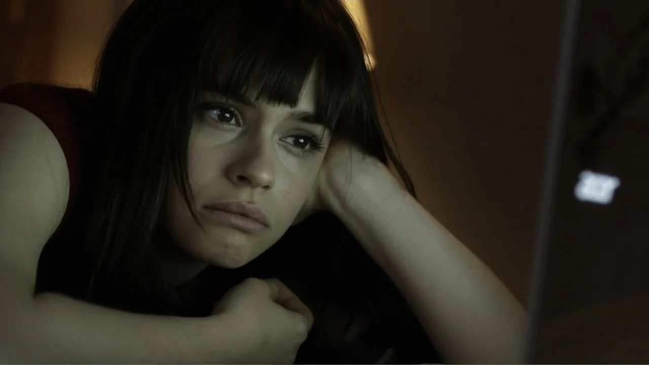 Like.Share.Follow. (2017) movie still: closeup — A dark indoor space is illuminated by the light from a laptop screen. A young woman with dark hair…