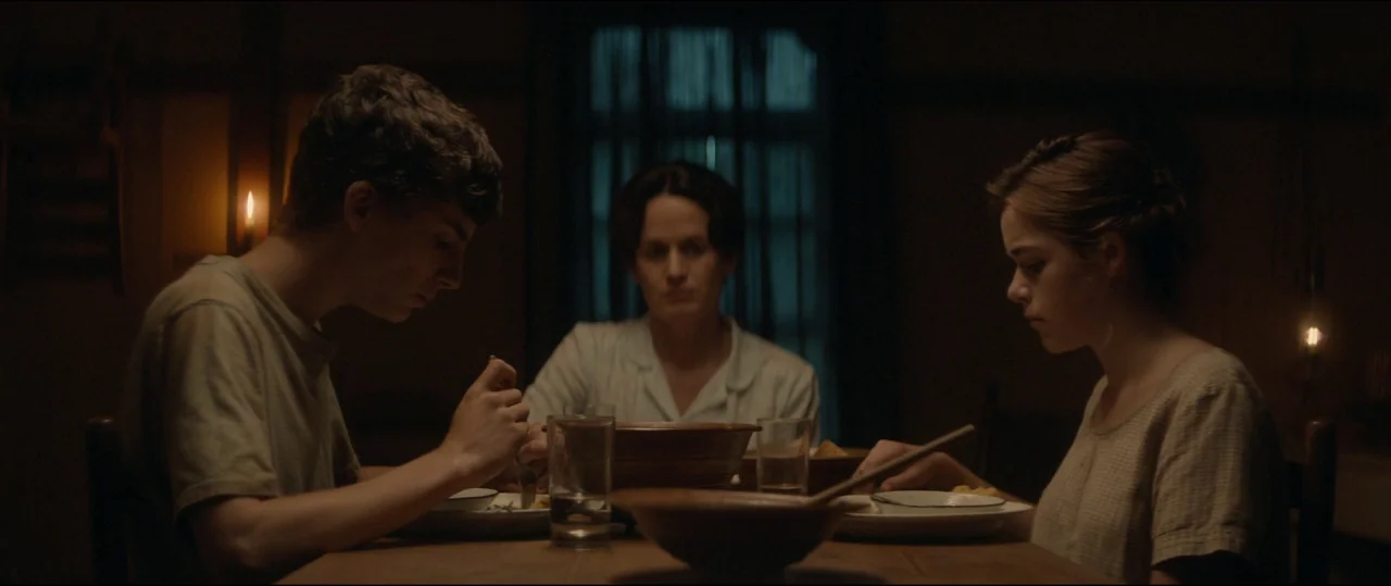 One & Two (2015) movie still: medium — A dimly lit room contains three people sitting around a simple wooden table. The group eats quietly while…