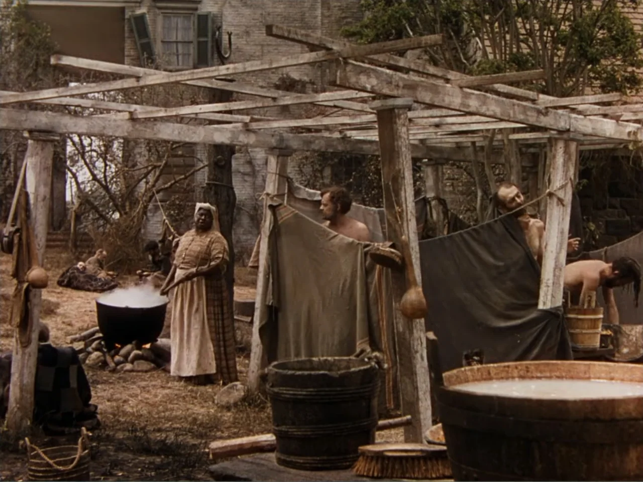 Gone with the Wind (1939) movie still: wide — A rustic outdoor laundry area features wooden drying frames and large boiling pots. A woman tends the…