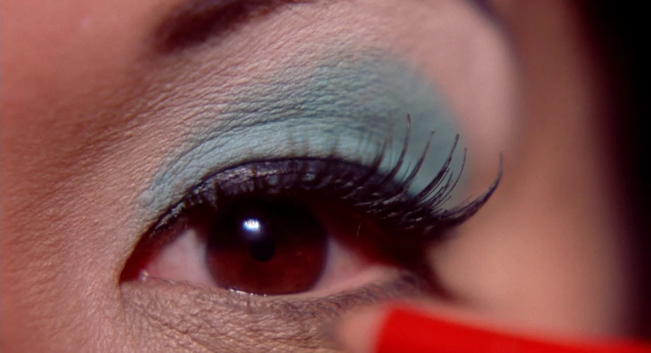 Viva (2007) movie still: closeup — A close-up view focuses on an eye with bright turquoise eyeshadow applied to the lid. A red eyeliner pencil is…