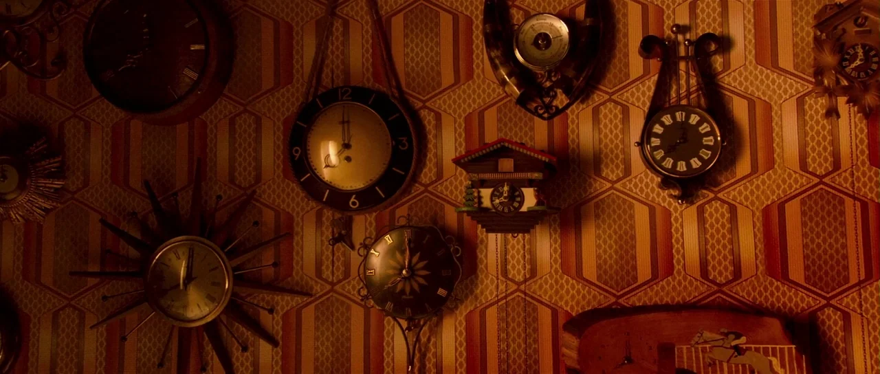 Bunny and the Bull (2009) movie still: establishing — A wall covered in 1970s patterned yellow and orange wallpaper is crowded with clocks. Various…