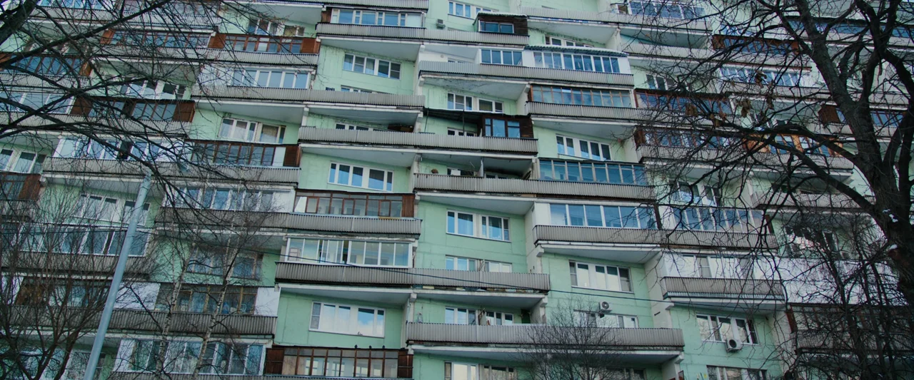 Anna (2019) movie still: establishing — A Soviet-era residential apartment block features repetitive balconies and mint-green painted exterior…