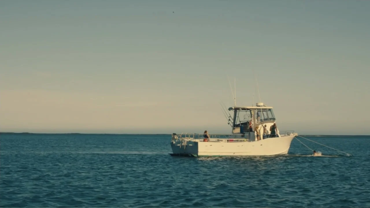 Camp X-Ray (2014) movie still: wide — A white cabin cruiser floats on a calm, expansive ocean during late afternoon light. Several people stand on…