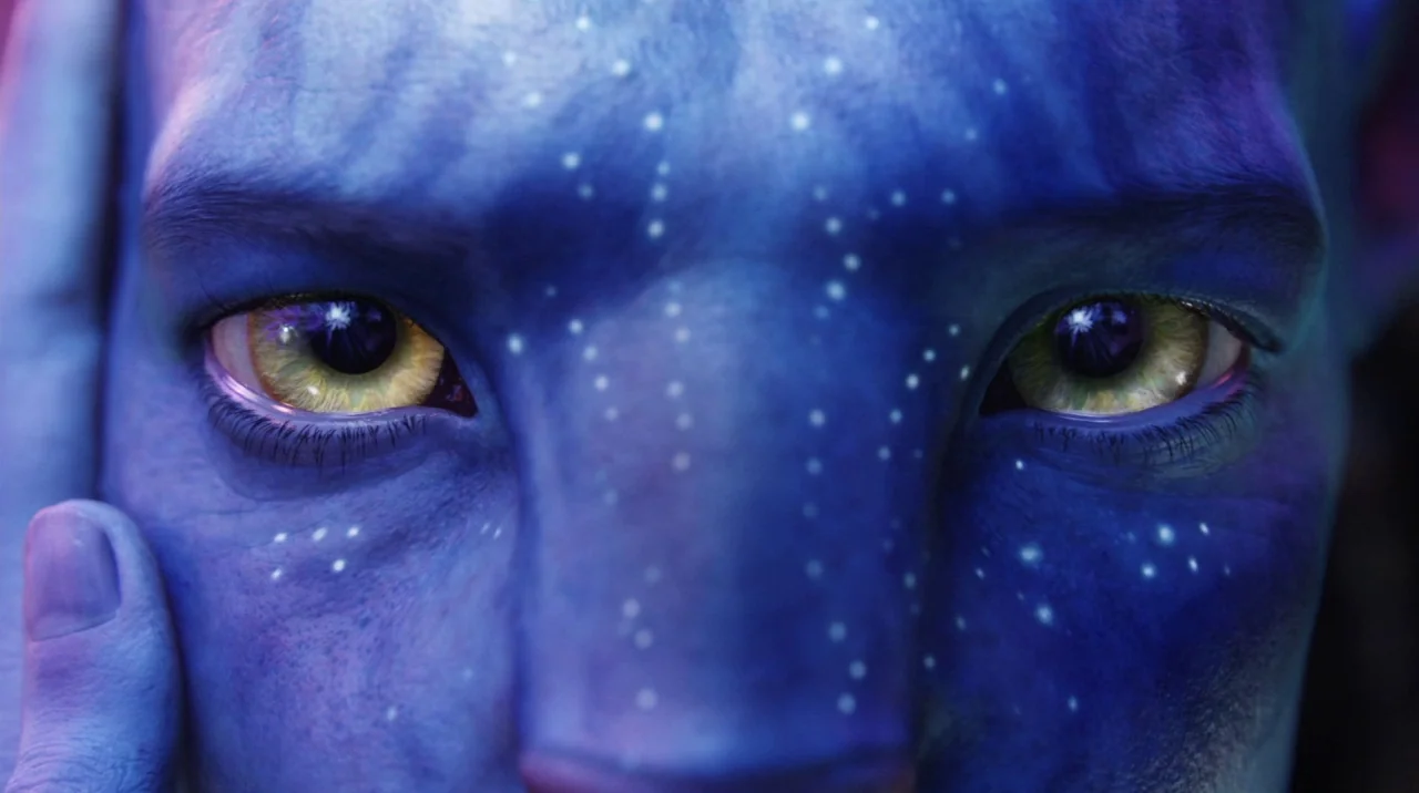 Avatar (2009) movie still: closeup — A close up view of an alien face with blue skin and bioluminescent dots. The alien stares ahead with striking…