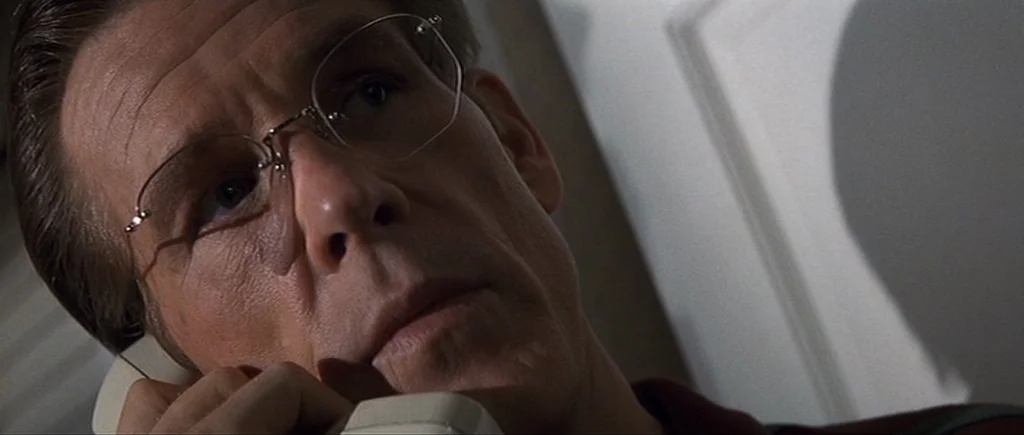 Cape Fear (1991) movie still: closeup — A man speaks on a telephone in a dimly lit, nondescript room. He looks downward while listening intently to…