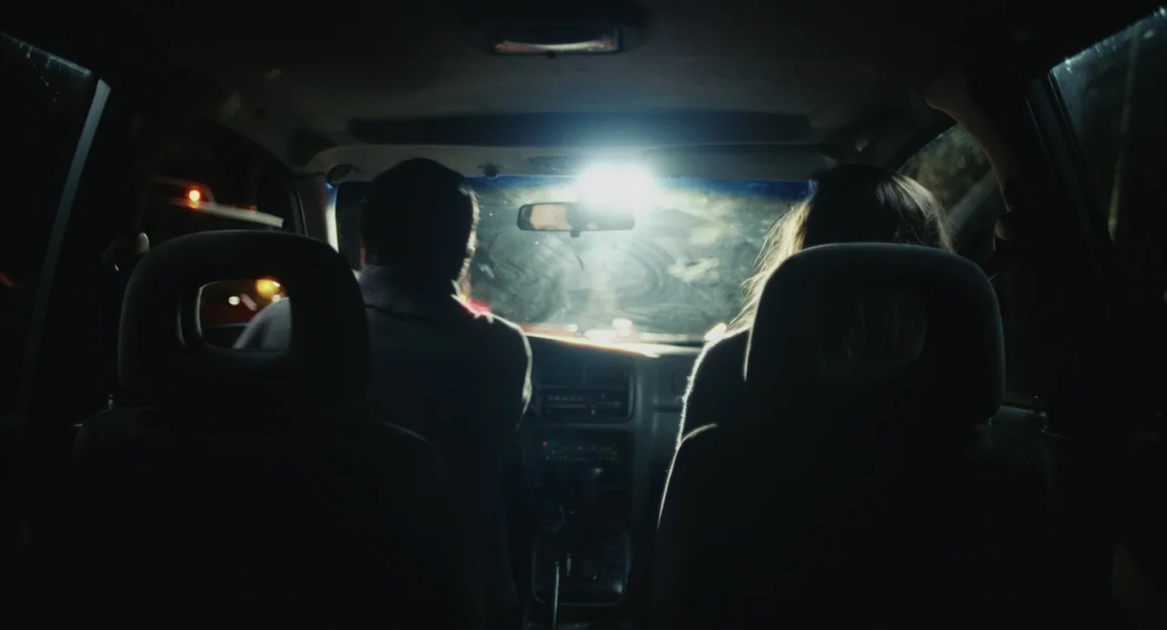 The Diary (1999) movie still: medium — The interior of a car at night seen from the back seat. A driver and passenger sit in front while light…