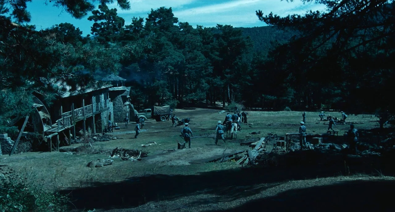 Pan’s Labyrinth (2006) movie still: wide — A rural military camp features a rustic stone building adjacent to dense pine woods. Soldiers in uniform…