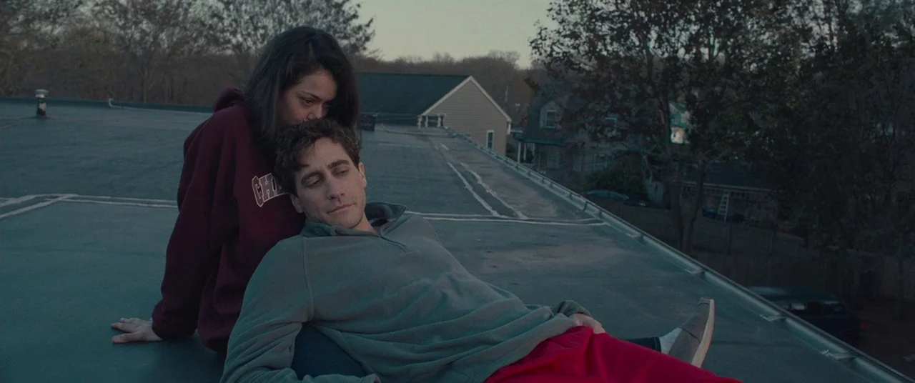 Stronger (2017) movie still: medium — A flat rooftop covered in dark roofing material overlooks suburban residential houses at dusk. A young man…
