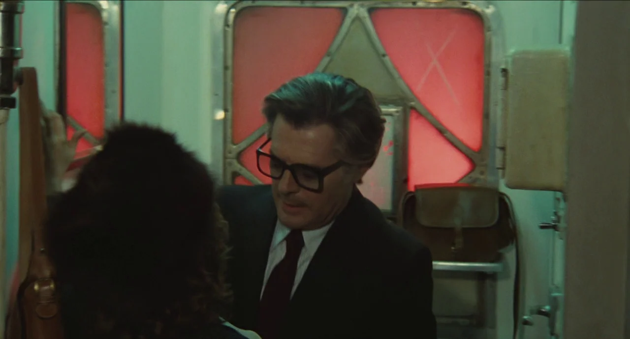 City of Women (1980) movie still: medium — A claustrophobic train compartment features metal walls and backlit red translucent panels. A man wearing…
