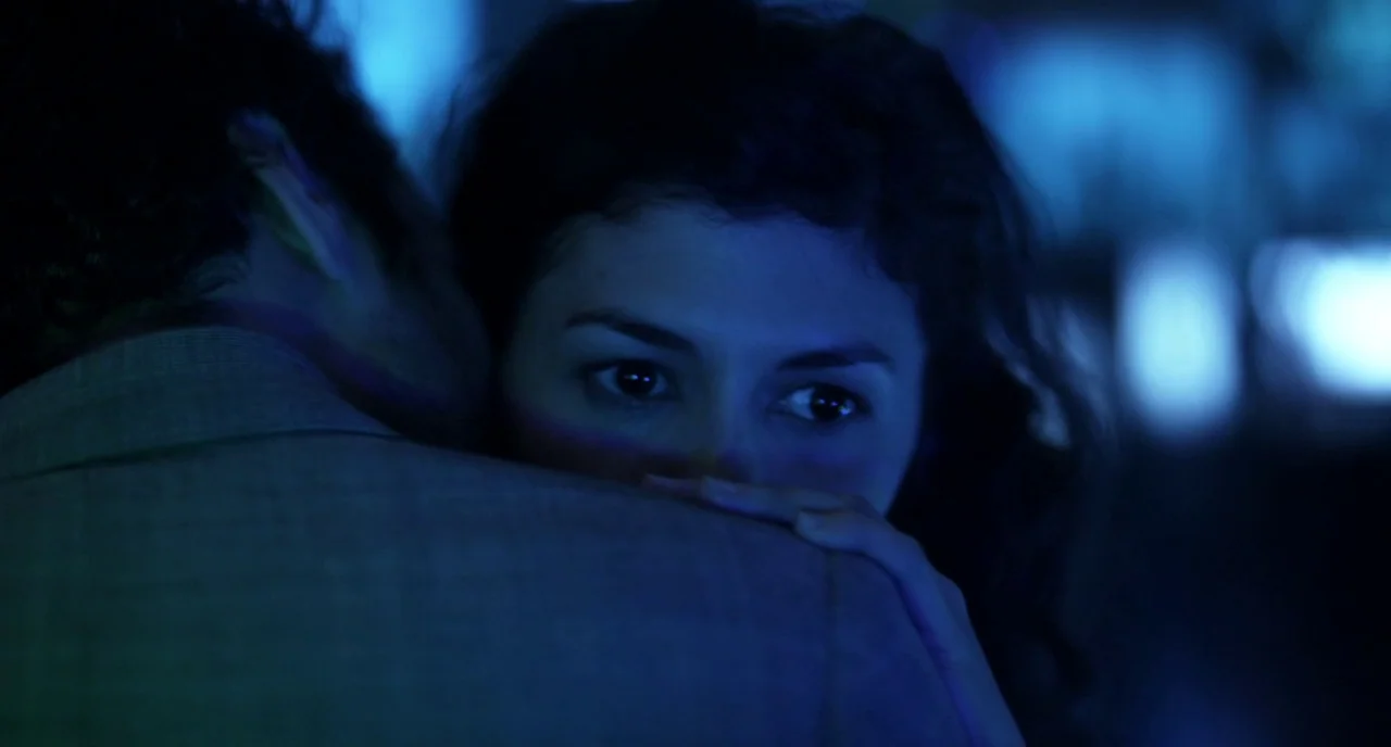 Mood Indigo (2013) movie still: closeup — A dark indoor space illuminated by vibrant blue neon light from surrounding sources. A woman rests her…