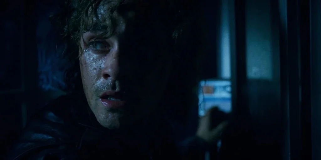 Stranger Things (2019) movie still: closeup — A dimly lit, shadowed room features cool blue light reflected onto a person. A young man with damp…