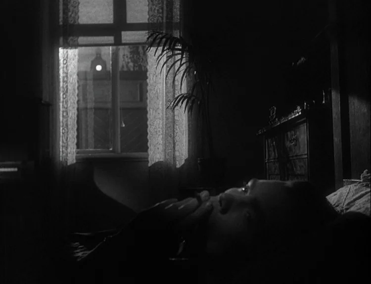 Music in Darkness (1948) movie still: closeup — A dark bedroom with a lit window and a potted plant silhouette. A woman rests on a bed and holds a…