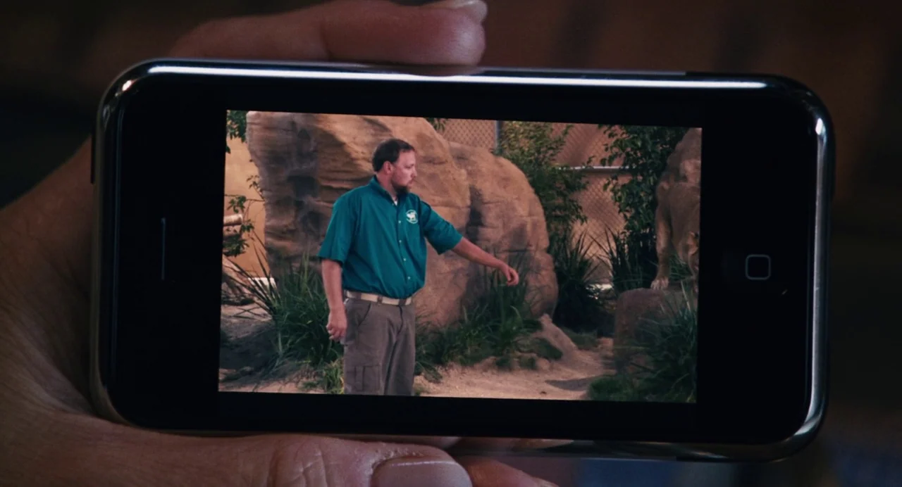 The Happening (2008) movie still: closeup — A man stands in an outdoor animal enclosure with large rocks and scattered grass. The man looks toward…