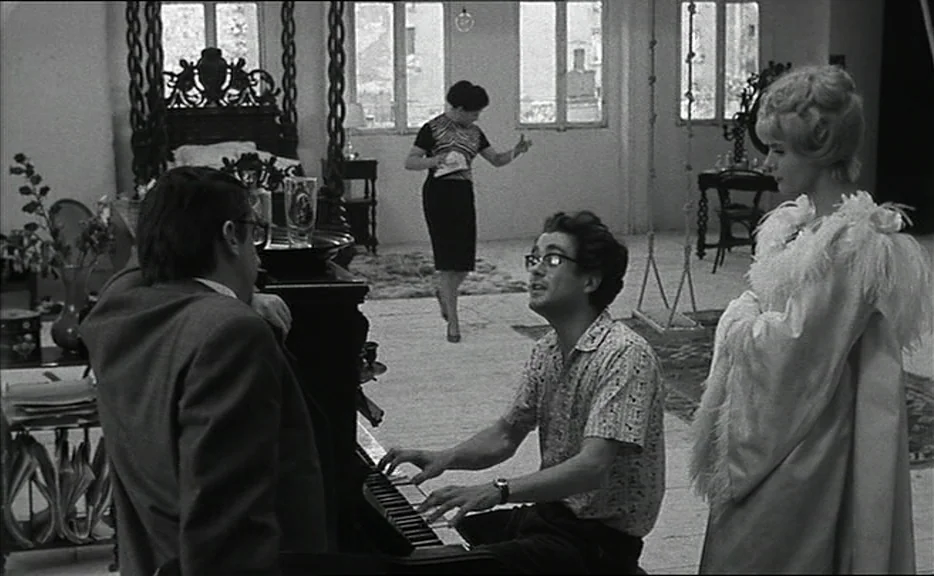Cléo from 5 to 7 movie still: fullbody — A spacious, bright apartment features a piano, a tall bed frame, and large windows. A man plays piano while…