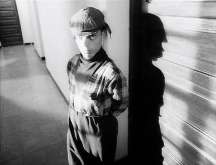 Even Dwarfs Started Small (1970) movie still: medium — A narrow residential hallway with a door at the far end. A man stands pressed against the…