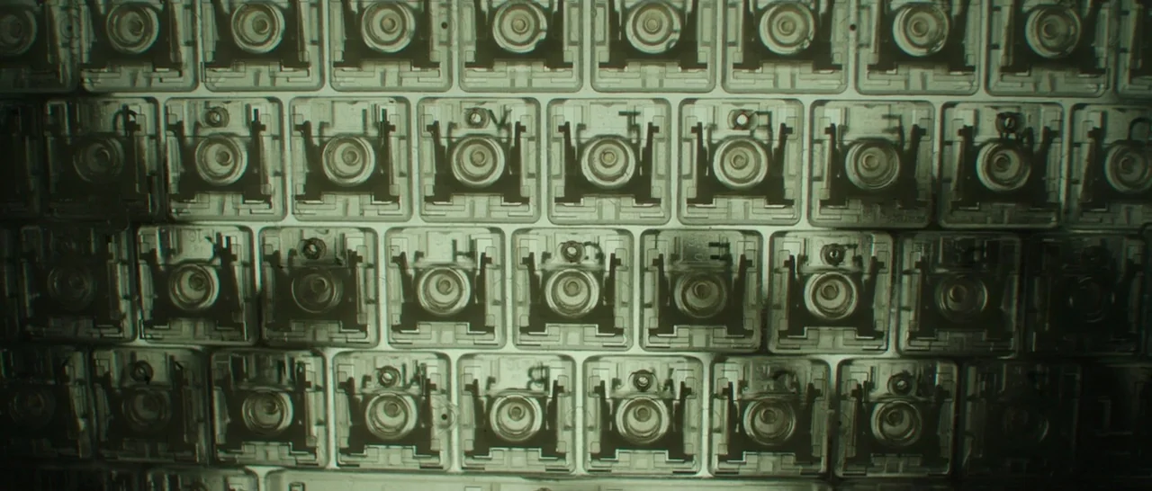 Blackhat (2015) movie still: closeup — A dense grid of transparent mechanical keyboard switches rests against a dark surface. The repeating square…
