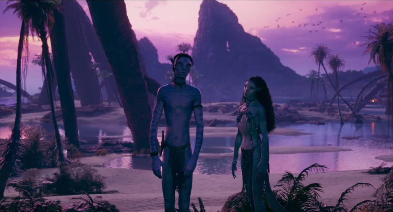 Avatar: The Way of Water (2022) movie still: fullbody — Two Na'vi figures stand on a sandy beach at the edge of shallow water. Towering rocky cliffs…