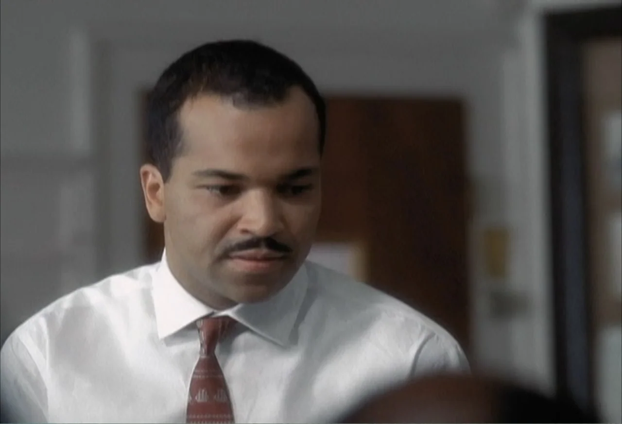 Boycott (2001) movie still: medium — An interior office space with blurred background furniture and light-colored walls. A man in a crisp white…