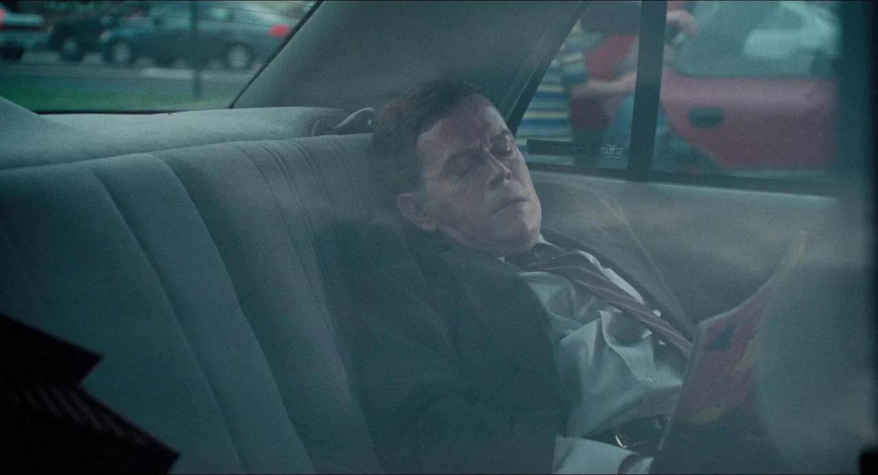 Happiness (1998) movie still: medium — A man sits in the back of a car during the day. He rests with eyes closed holding a small publication.