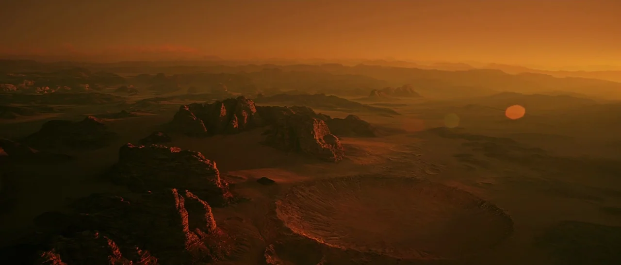 The Martian (2015) movie still: establishing — A vast, arid desert landscape features craggy rock formations and a prominent circular crater. The…
