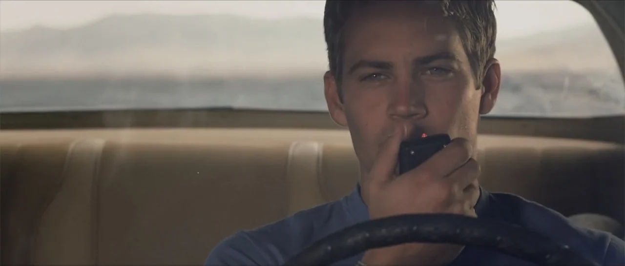 Joy Ride (2001) movie still: medium — A man drives a vehicle through a desert landscape visible through the rear window. The man holds a black…