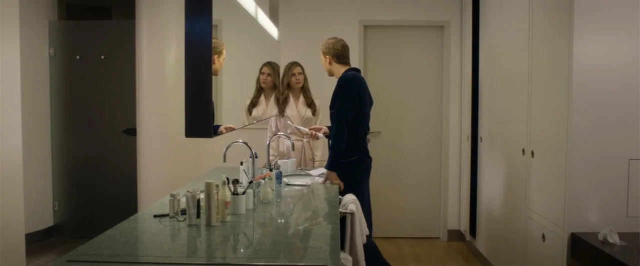 Heartburn (1986) movie still: medium — A modern, minimalist bathroom features a green stone double vanity and white cabinetry. A man in a dark robe…