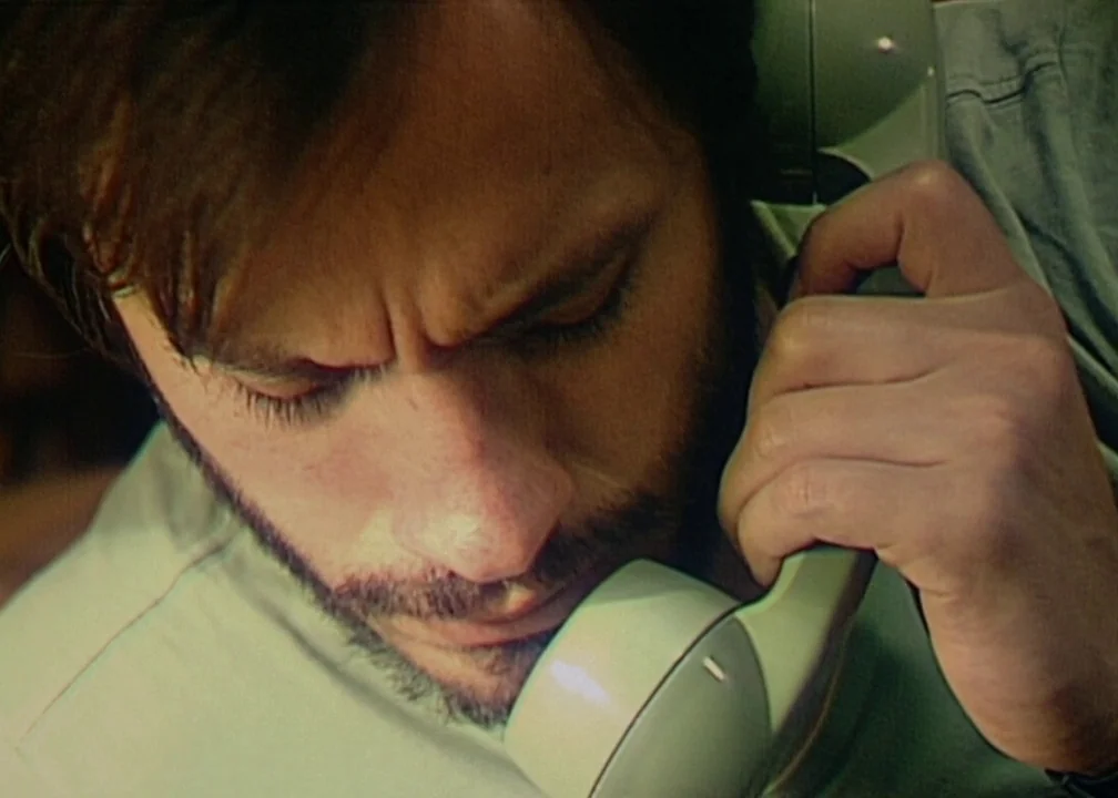 No (2012) movie still: closeup — A man holds a telephone handset against his ear while looking downward. The close framing focuses on the man's face…