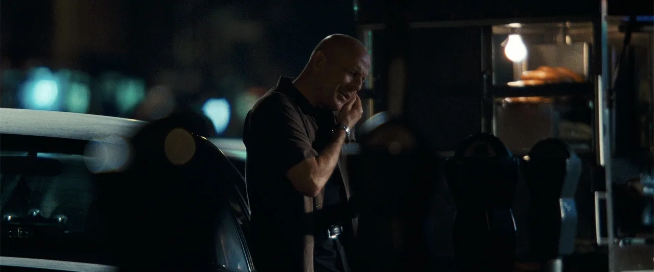 Cop Out (2010) movie still: medium — A nighttime city street at night featuring a car parked near a food vendor cart. A man stands alone next to the…