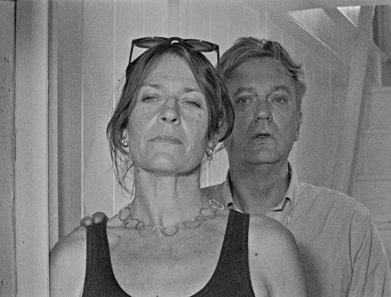 Bait (2019) movie still: medium — A woman and a man are positioned in a narrow interior stairwell space. The woman stands in the foreground while…